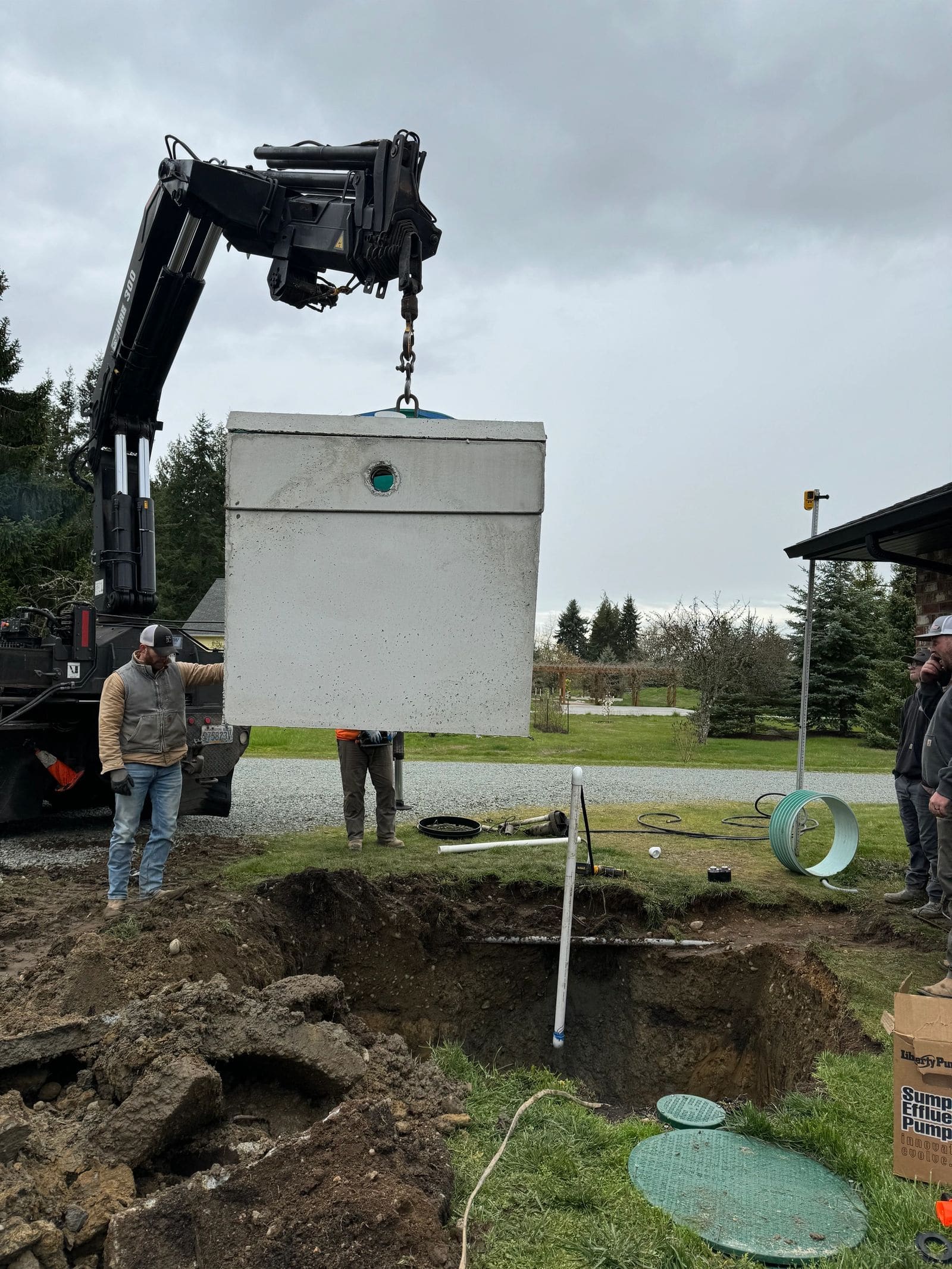 A concrete septic tank suspended from a crane over its excavation.