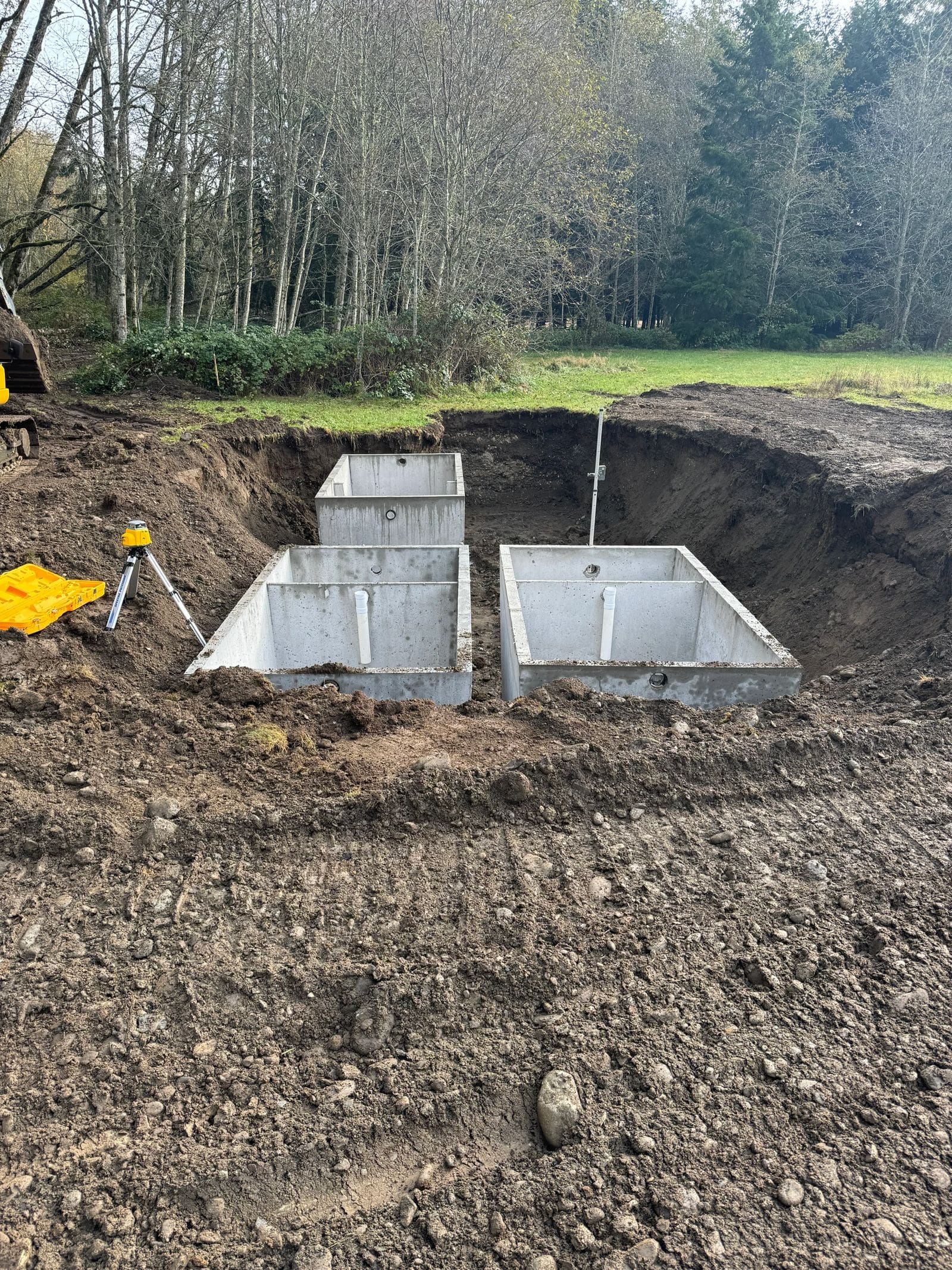 Three new concrete septic tanks set in an open excavation.